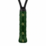 Dark green custom tennis overgrip printed with a repeating gold "SB" monogram, close-up on a racket handle.