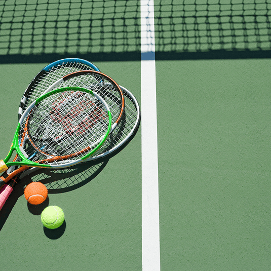 Four stacked tennis rackets on a tennis court with two tennis balls.